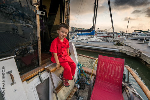 Portrait of young boy in red outfit sitting on boat, portrait.