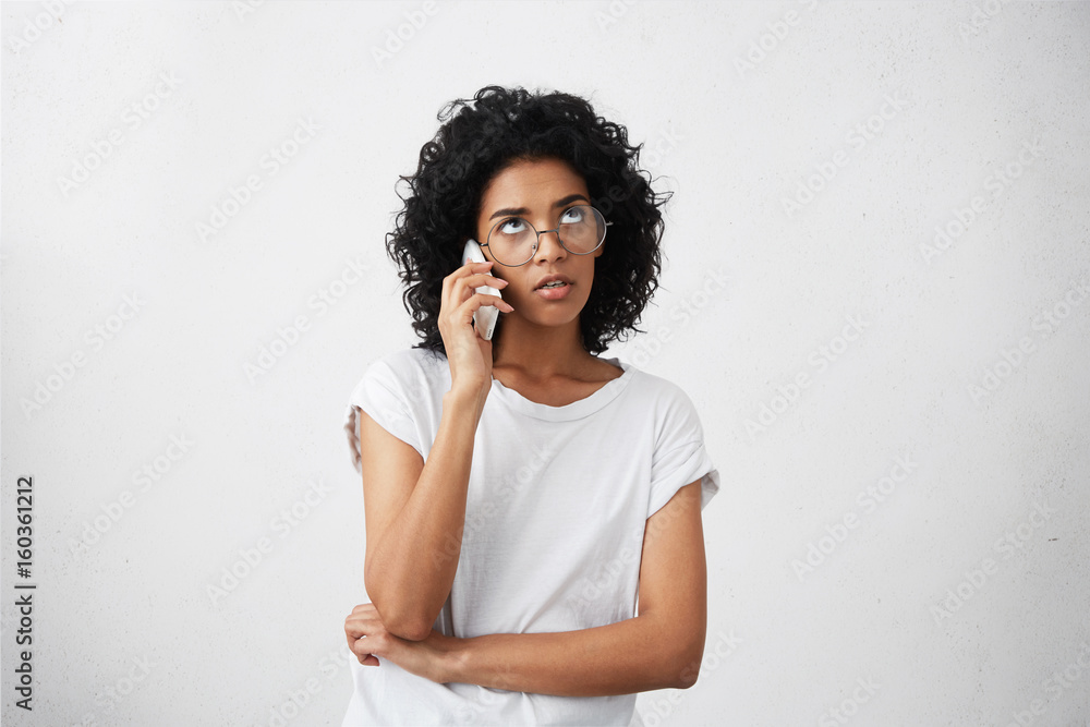Waist up portrait of concerned African businesswoman deciding her problems over mobile phone dressed casually while being at home during weekends. Busy African woman chatting over smartphone Waist up portrait of concerned African businesswoman deciding her problems over mobile phone dressed casually while being at home during weekends. Busy African woman chatting over smartphone