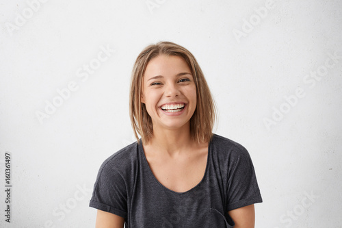 Attractive woman with short fair hair being very glad smiling with broad smile showing her perfect teeth having fun indoors. Joyful excited cheery femlae rejoicing after being proposed to marry photo