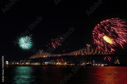Colorful fireworks explode over bridge, reflection in water. Montreal’s 375th anniversary. luminous colorful interactive Jacques Cartier Bridge. Bridge panoramic colorful silhouette by night.