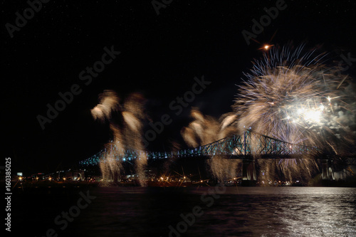 Colorful fireworks explode over bridge, reflection in water. Montreal’s 375th anniversary. luminous colorful interactive Jacques Cartier Bridge. Bridge panoramic colorful silhouette by night.