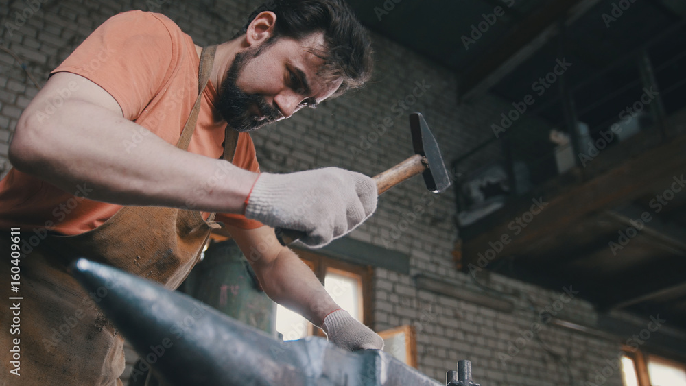 Muscular blacksmith in forge hammering steel products Muscular blacksmith in forge hammering steel products