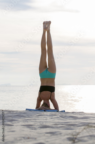 Fototapeta Naklejka Na Ścianę i Meble -  Young woman practices yoga on a beach at sunset