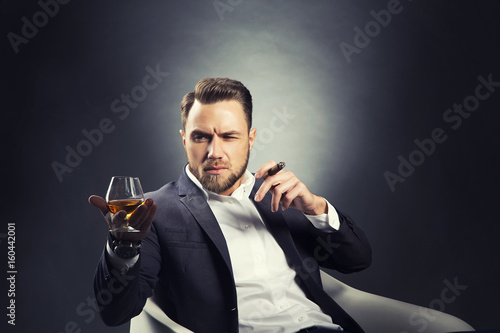 Portrait of handsome man drink cognac with cigar over dark studio background