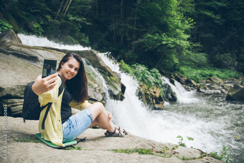 woman taking picture on the phone of waterfall on background