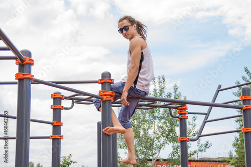 Teenager with dreadlocks sits on the bar on the playground