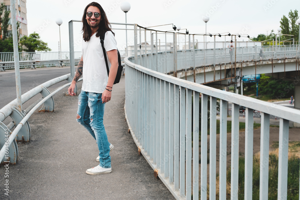 Stylish hipster model with long hair lifestyle in the street. Dressed in a white T-shirt and torn blue jeans in the city