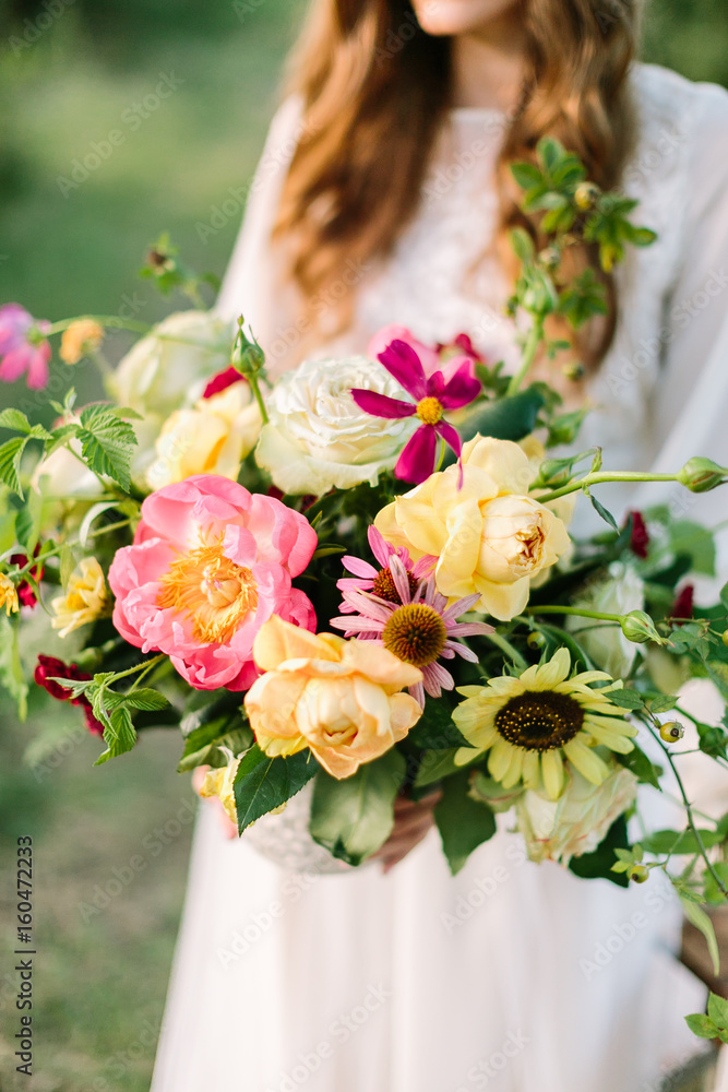 wedding, floral design, fashion, celebration concept - beautiful bouquet of ornamental flowers tender avalanches, peonies and marsala colored carnations in hands of bride in white dress