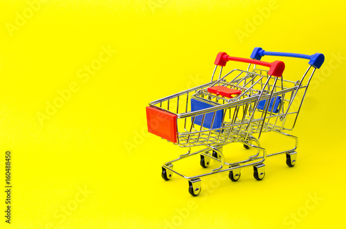 mini red and blue color supermarket shopping cart on yellow background, holiday sale and online shopping concept, selective focus, copy space