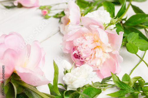 Close up of pink and white flowers on wooden table. Peonies and wild roses. High key, copy space.