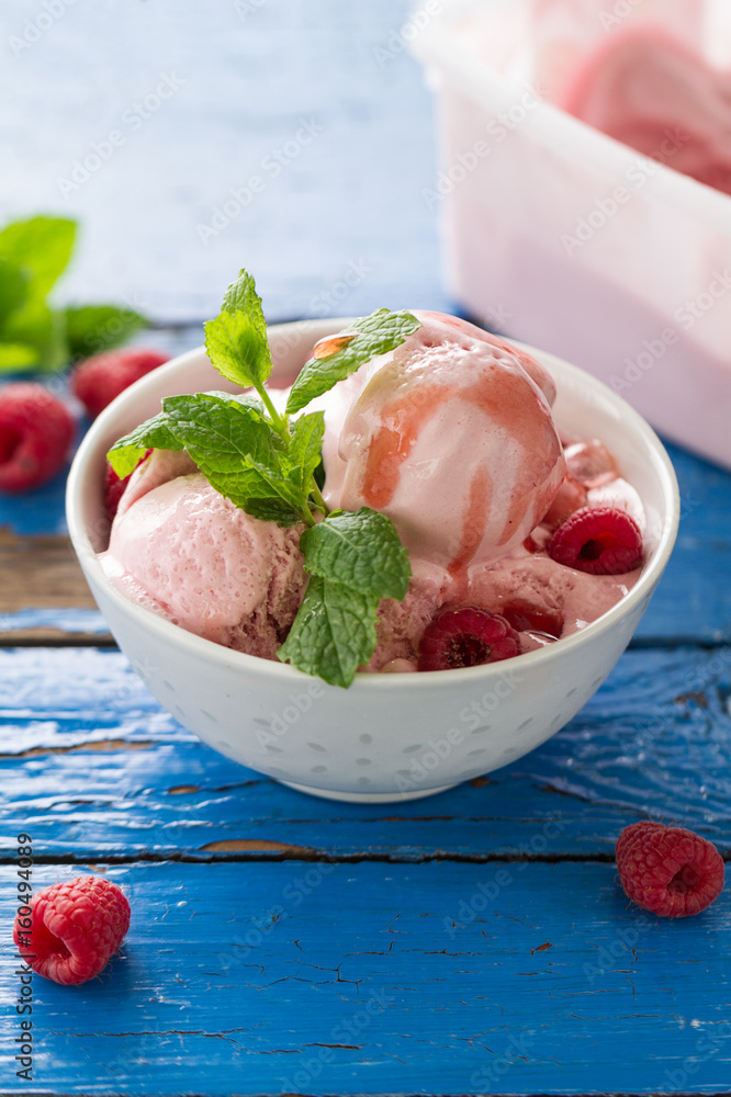 Tasty vanilla ice scoops with strawberry jam and mint in bowl on blue wooden rustic table. Closeup. Tasty vanilla ice scoops with strawberry jam and mint in bowl on blue wooden rustic table. Closeup.