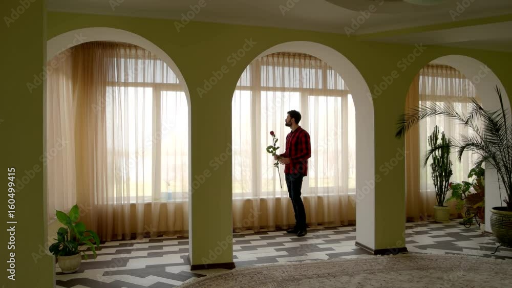 Man holding rose near window. Guy with flower standing indoor. Waiting for girlfriend. Man holding rose near window. Guy with flower standing indoor. Waiting for girlfriend.