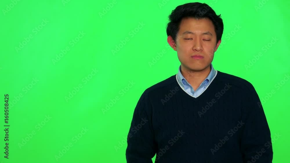 A young Asian man shakes his head disapprovingly, his arms folded across his chest - green screen studio A young Asian man shakes his head disapprovingly, his arms folded across his chest - green screen studio