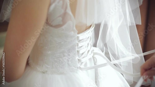 Morning bride. maid of honor helping the bride with her dress. the bride's lace up dress. Bridesmaid tying bow on wedding dress. Woman's hands lace up silk ribbon on bride's corset. Helping to lace up