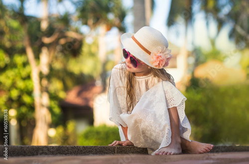 A nice beautiful girl in a hat and sunglasses relaxing by the pool relaxes