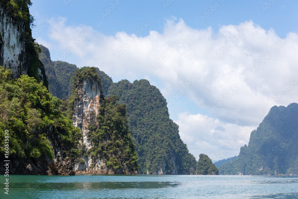 Landscape with vertical rocks and dense tropical vegetation on background of the blue sky and clouds in the lake Ratchaprapha