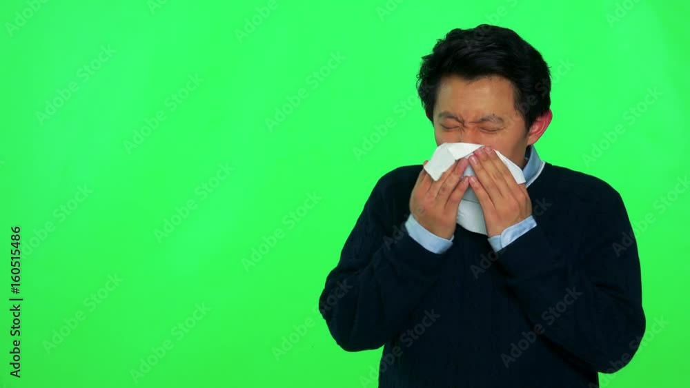 A young Asian is sick and blows his nose into a paper tissue - green screen studio A young Asian is sick and blows his nose into a paper tissue - green screen studio