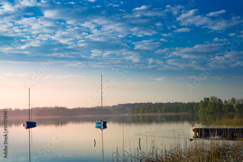 Yachts float on the calm waters of the lake. Early morning. Masuria, Poland .