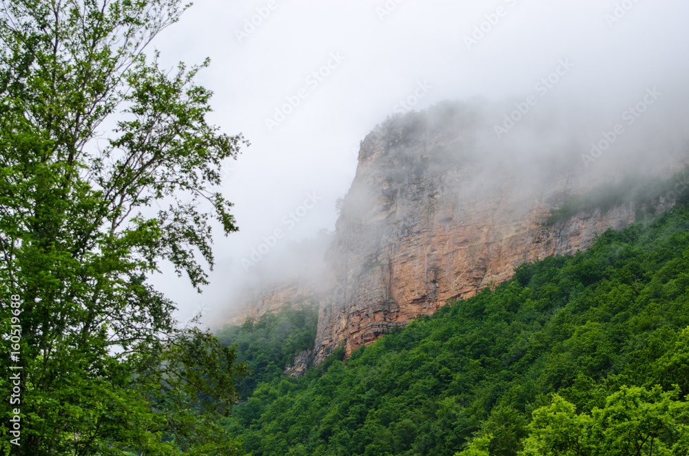 Haze fog over the rocks. Cloud over the mountainin Caucasus. Green leaf forest. Mezmay and Guamka