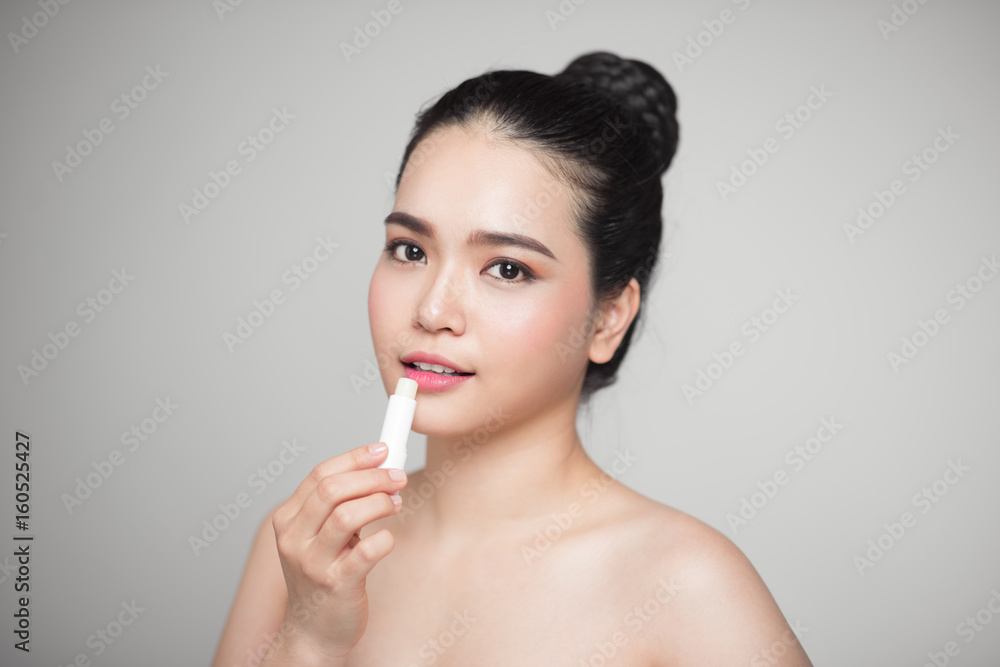 Asian woman applying hygienic lip balm over grey background Asian woman applying hygienic lip balm over grey background