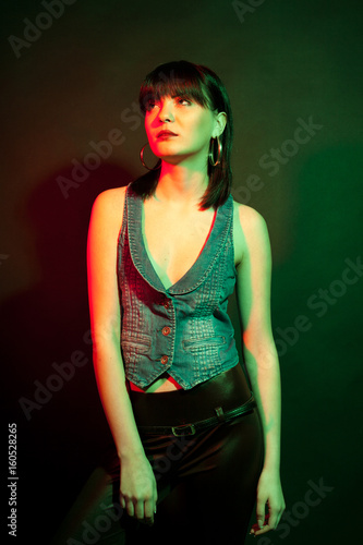 Stylish woman in leather pants in red and green light. Studio photo. Beauty and fashion