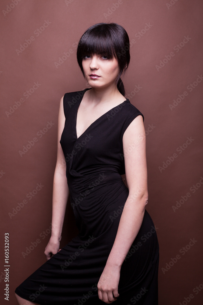 Woman in long black dress on brown background in studio photo. Beauty and fashion. Model test