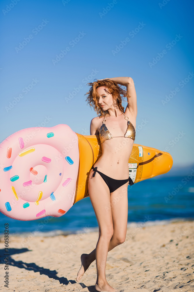 Portrait of a beautiful young sexy sexy red-haired curly-haired girl in a swimsuit against the background of the island of palma de mallorca spainan inflatable mattress in the form of an ice cream