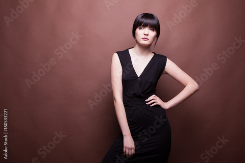 Gorgeous woman in long black dress on brown background in studio photo. Beauty and fashion. Model test