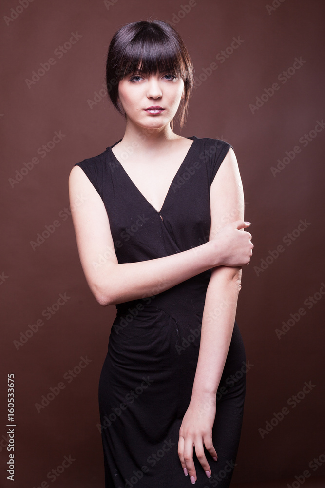 Obraz premium Sensual woman in long black dress on brown background in studio photo. Beauty and fashion. Model test