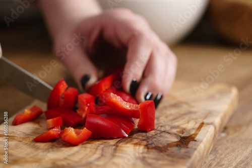young female hands chopping red bell pepper on kitchen table