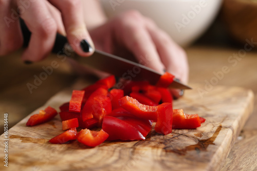 young female hands chopping red bell pepper on kitchen table