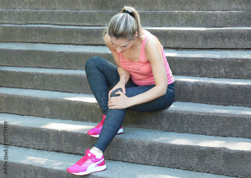 Young woman suffering from pain in leg while sitting on steps outdoors