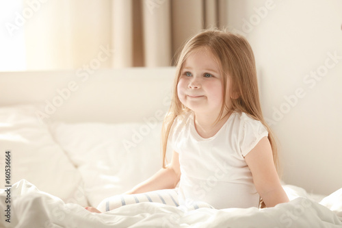 Morning of cute little girl sitting on bed at home