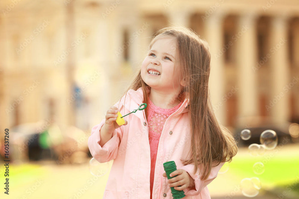 Cute little girl playing with soap bubbles outdoors on spring day