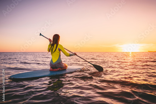 Girl on stand up paddle board, quiet sea with warm sunset colors. Relaxing on ocean photo