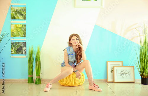 Beautiful young woman sitting on pouf at home