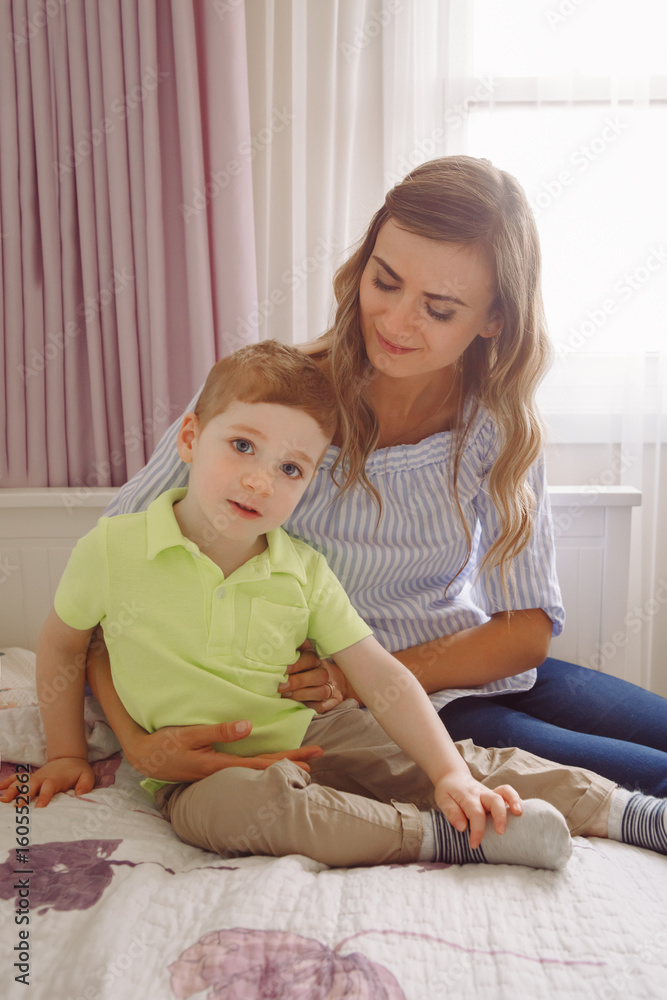 Funny group portrait of beautiful young white Caucasian mother and toddler child boy, playing together on bed in bedroom, having fun, natural candid family lifestyle