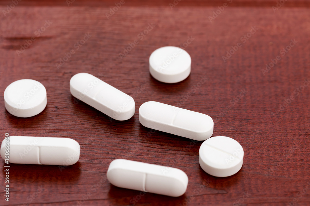 Various white pills on wooden table