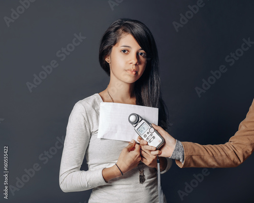 Portrait of beautiful hispanic latin brunette young woman in studio holding white paper and flash meter, measuring light, on plain black background