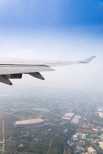 Flying into blue sky and city building on ground and Wing of airplane with skyline top view as look from window airplane, during flight space for text message, frame or traveling idea concept