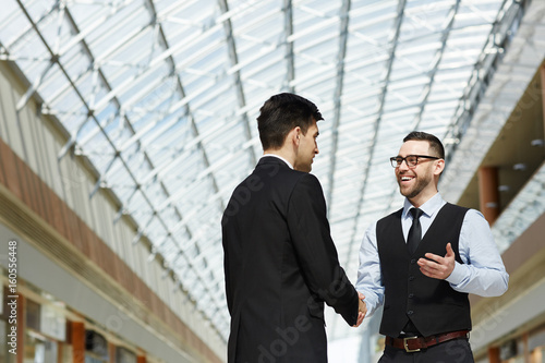 Portrait of modern entrepreneur greeting business partner by handshake and smiling in office building under glass roof, copy space