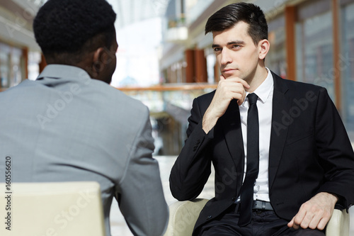 Portrait of young successful businessman talking to African-American business partner, discussing work in modern office building