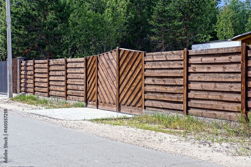 коричневые ворота и забор перед асфальтированной дорогой в солнечный день