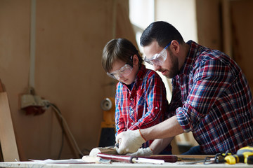 Little trainee learning to woodcarve while his father teaching him