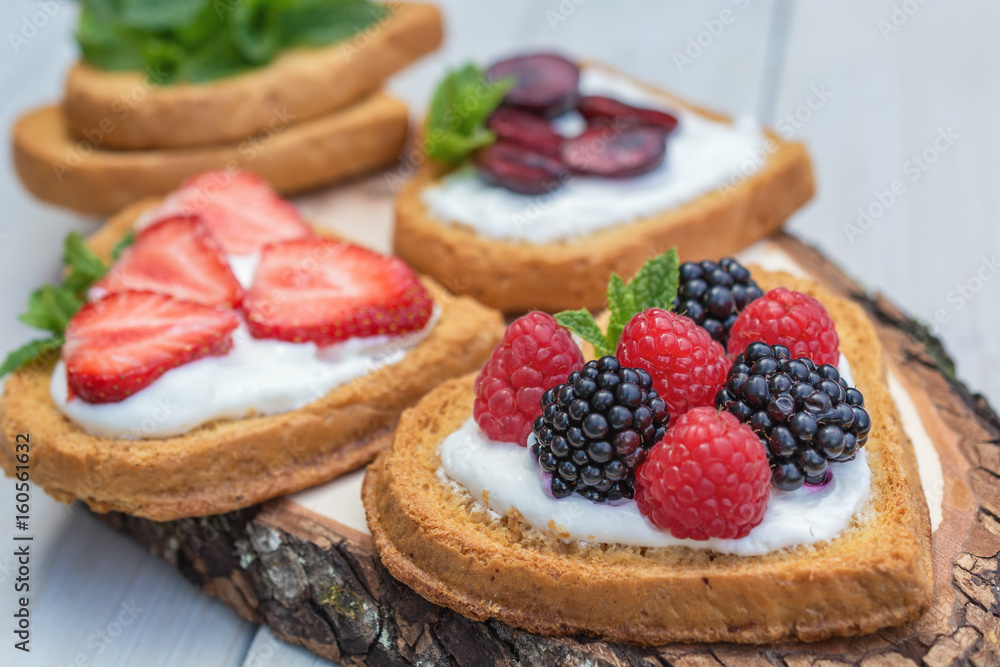 Heart shaped biscuits spread with quark, strawberries, blackberries, raspberries, cherries and a twig of mint presented on a tree disk Heart shaped biscuits spread with quark, strawberries, blackberries, raspberries, cherries and a twig of mint presented on a tree disk