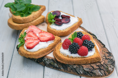 Heart shaped biscuits spread with quark, strawberries, blackberries, raspberries, cherries and a twig of mint presented on a tree disk