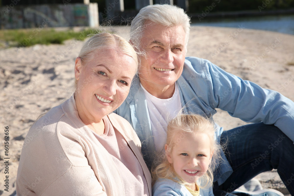 Happy grandparents with little girl sitting on river bank Happy grandparents with little girl sitting on river bank