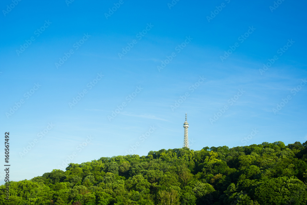 Petrin Lookout Tower ( Petrinska rozhledna ), Prague, Czech Republic / Czechia - tall building on the top of the hill. Green trees around it. Minimalist composition with blue sky as copy space
