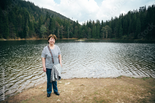 Aged beautiful woman standing on the bank of the mountain lake surrounded by forest. Travel concept © Iryna Budanova