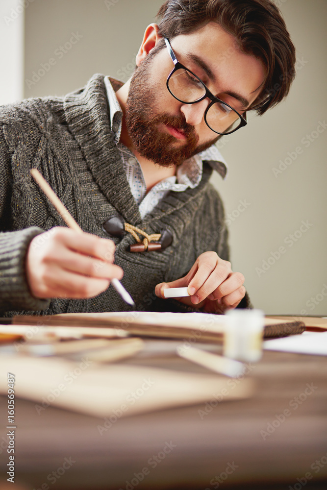 Bearded painter in eyeglasses and sweater drawing by workplace Bearded painter in eyeglasses and sweater drawing by workplace